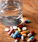 Close-up of various colourful pills next to glass of water on wooden surface