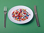 Tablettenmix auf einem Teller, Messer, Gabel, grüner Untergrund