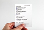 Close-up of hand holding travel checklist for vacation against white background