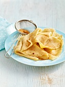 Crepes and strainer with cinnamon powder on plate