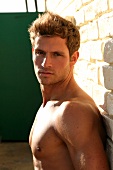 Portrait of handsome shirtless blonde man, leaning against wall