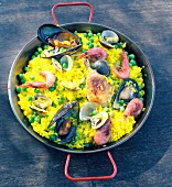 Paella in einer massiven Pfanne auf einem Holztisch stehend