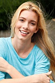 Portrait of beautiful blonde woman with long hair wearing blue top, smiling