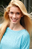 Portrait of beautiful blonde woman with long hair wearing blue top, smiling