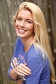 Portrait of happy blonde woman with long hair wearing blue top, arms crossed, smiling