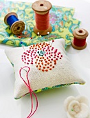 Creme pin cushion with flower motif , needle and bobbins on side