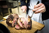 Close-up of man's hand cutting roasted beef on chopping board