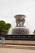 Man standing near the fountain with statues in Vigeland Sculpture park in Oslo, Norway