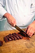 Close-up of chef cutting baked beef liver into slices with knife