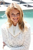 Portrait of blonde woman wearing white turtleneck sweater standing on beach, smiling