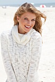Portrait of blonde woman wearing white turtleneck sweater standing on beach, smiling
