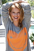 Portrait of carefree blonde woman wearing gray t-shirt laughing with arms on head 