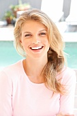 Portrait of happy blonde woman wearing pink sweater sitting, smiling