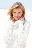 blonde Frau in weißem Rolli lächelt in Kamera, am Strand