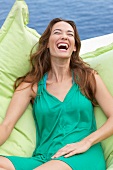 Portrait of happy brown haired woman wearing green dress sitting on green cushion, smiling