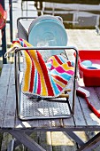 A plastic washing-up bowl, a drainer and a colourful crocheted tea towel on a wooden table outside