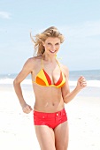 blonde Frau im gelb-roten Bikini und Hot Pants in rot, am Strand