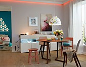 A dining room with a round table, a strip light and an illuminated sideboard