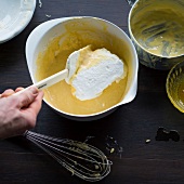 Close-up of man's hand mixing cheese souffle, cream and egg whites in bowl