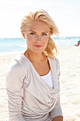blonde Frau im hellen Shirt lächelt in Kamera, am Strand