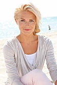 blonde Frau im hellen Shirt lächelt in Kamera, sitzt am Strand