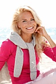 blonde Frau im Pulli in pink, lächelt in Kamera, am Strand