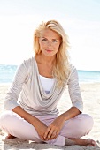 blonde Frau im hellen Shirt lächelt in Kamera, sitzt am Strand