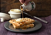 Maple syrup being poured on apple cinnamon waffles