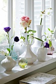 Summer flowers in various white vases on a window sill