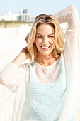 Blonde woman with long hair in a light sweater on the beach