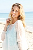 Blonde Frau mit langen Haaren in hellem Pulli am Strand