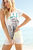 Blonde, sportliche Frau mit langen Haaren im T-Shirt am Strand