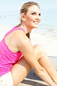 Blonde Frau mit langen Haaren im pinken Shirt relaxt am Strand