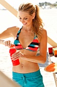 Blonde woman with long hair in a bikini and shorts, with a bottle
