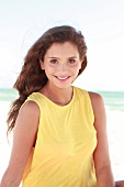 Woman with long dark hair in a yellow shirt on the beach