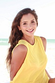 Woman with long dark hair in a yellow shirt on the beach