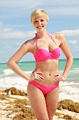 Blonde Frau mit kurzen Haaren im pinkfarbenem Bikini am Strand