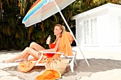 Blonde Frau mit Zopf relaxt auf Liege am Strand unterm Schirm