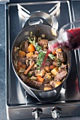 Venison ragout being made: red wine being poured over vegetables and meat