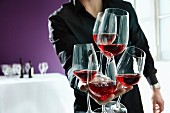 A waiter holding lots of glasses of red wine