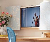A vase of roses on a console table in front of a wall-mounted television behind wallpapered sliding doors