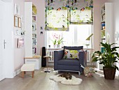 An armchair in a sunny reading corner flanked by white bookshelves and floral-and-bird-patterned folding blinds