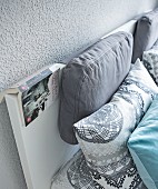Dicke Kissen am schlichten Kopfteil eines Doppelbetts vor grau getönter Wand