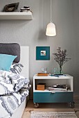 A pendant lamp over a rolling bedside table next to a bed in a bedroom with grey walls