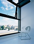 White shell stool in designer style on a white floor in front of a bank of windows with a view