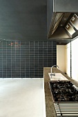 Langgestreckte Küchenzeile und raumhohe schwarze Wand teils gefliest
