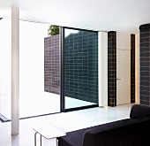 Black sofa in front of an open patio door and view of a black tiled wall in front of a white floor