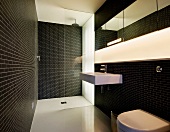 Dramatic bath with black tiled walls and recessed strip lighting in the wall over the wash basin