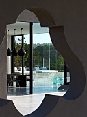 View through wall opening with organic shape of dining area with large pendant lights and terrace with concrete sunbathing platform