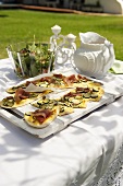 Tarte flambée with Parma ham and courgette on a table in a garden